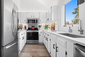Une cuisine moderne avec des meubles blancs, des appareils en acier inoxydable et une fenêtre donnant sur l’extérieur.