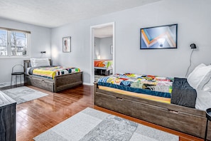 Two beds with colorful quilts, a dresser, and desk area in a calm and inviting space.