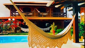A hammock by a pool with a traditional building in the background. - Casa com Piscina em Penha - Beto Carrero (Penha)