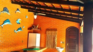 A kitchen with a brick wall, wooden tables, a refrigerator, and a door with a curtain. - Casa com Piscina em Penha - Beto Carrero (Penha)