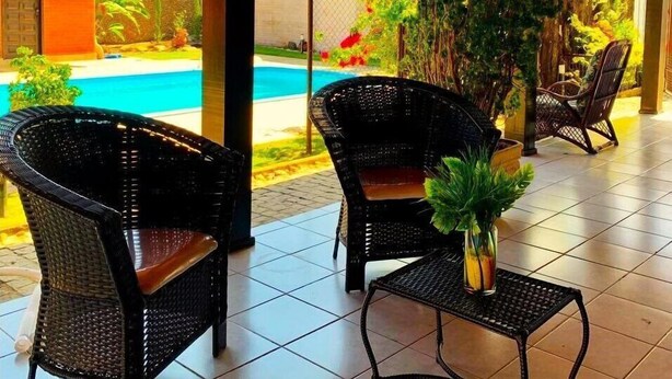 An outdoor patio area with wicker furniture, a small table, and a potted plant. - Casa com Piscina em Penha - Beto Carrero (Penha)