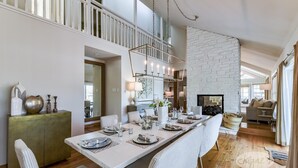 Comedor con una mesa larga dispuesta para seis comensales, sillas blancas y una lámpara colgante.