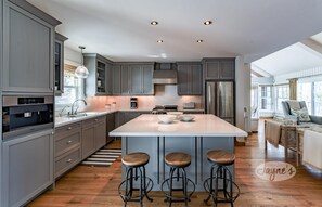 Una cocina moderna con armarios grises, una isla central con taburetes y un ventanal grande.