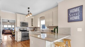 A spacious kitchen with white cabinets, a large island with stools, a microwave, and a ceiling fan. - Adorable Atlanta gem near downtown with WiFi, backyard, & excellent location (Atlanta)