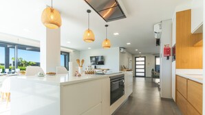 A modern kitchen with a central island, pendant lighting, and a view of the outdoors. - Villa de la Ponte by Atlantic Holiday (Estreito Calheta)