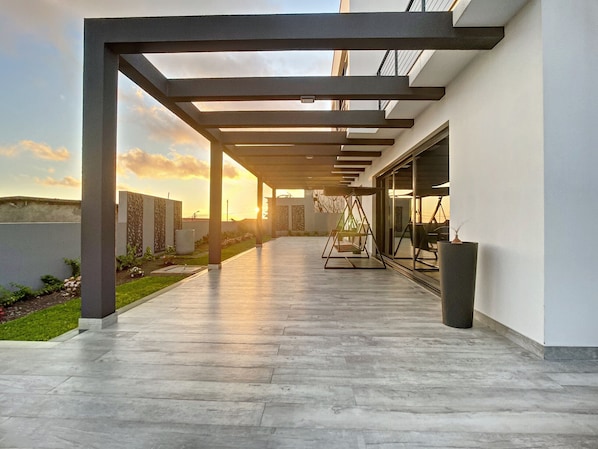 A covered outdoor area with a patio, a swing set, and a view of the sunset.