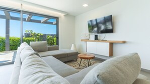 A modern living room with a large sectional sofa, a flat-screen TV mounted on a wooden shelf, and a glass door leading to a balcony. - Villa de la Ponte by Atlantic Holiday (Estreito Calheta)