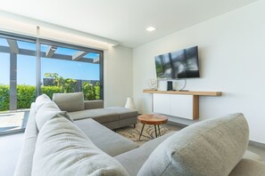 Ein modernes Wohnzimmer mit einer großen Eckcouch, einem flachbildfernseher, der an einem Holzboden montiert ist, und einer Glastür, die auf einen Balkon führt.