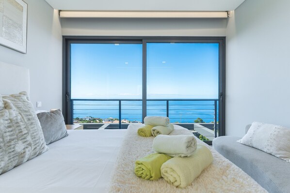 Une chambre moderne dotée d’une grande porte-fenêtre coulissante donnant sur un balcon avec vue sur la mer.