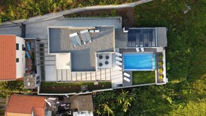 An aerial view of a modern house with a rooftop pool, outdoor seating area, and a small garden.