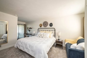 A bedroom with a large bed, a desk, a chair, a bedside table, and a couch. - Tranquility Cove at Smith Mountain Lake —Your Home Away From Home! (Moneta)