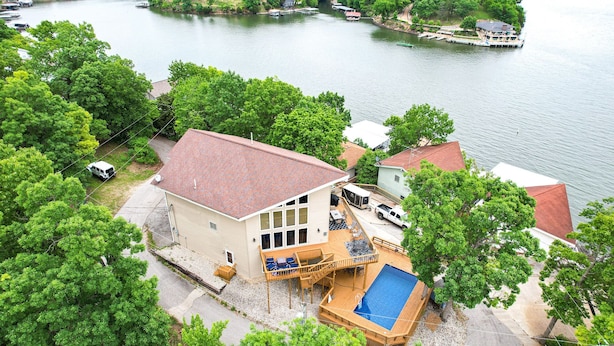 Une maison dotée d’une grande terrasse et d’une piscine, entourée d’une végétation luxuriante et bordée d’un lac.