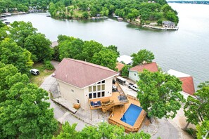 Una casa con un amplio deck y piscina, rodeada de vegetación exuberante y un lago.