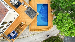 Une piscine sur le toit, dotée d’une terrasse en bois, d’un espace salon couvert et offrant une vue sur les arbres environnants.