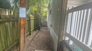 A narrow pathway with a wooden fence on one side and a metal gate on the other, leading to a building with a green exterior. - Biloxi Shuckers walk to the Blue Wahoos stadium!Close to Navy Base & Beaches. (Pensacola)