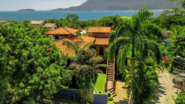Una propiedad costera con edificios de tejados terracota, abundante vegetación y una vista despejada del mar y las montañas.