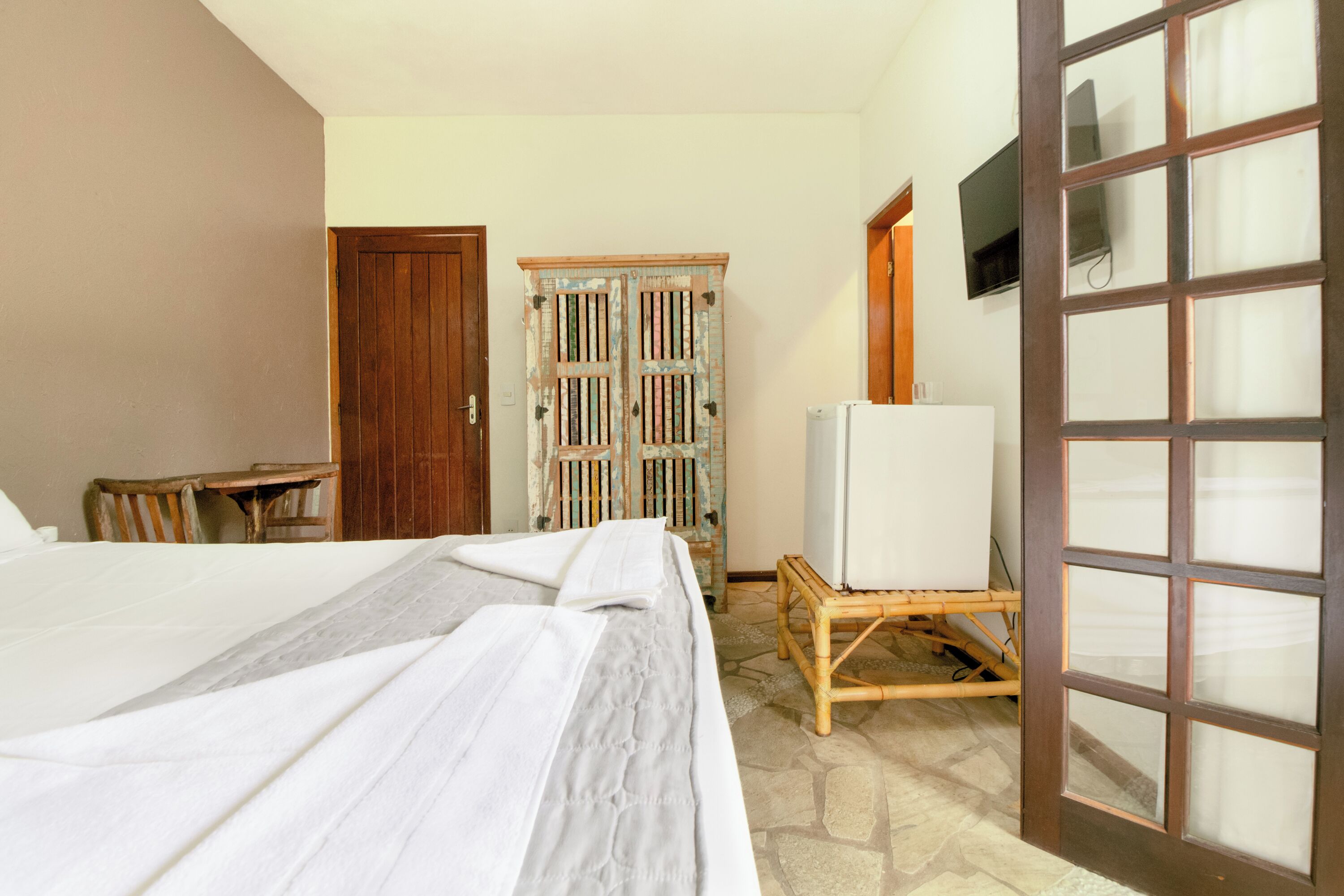 A hotel room with a bed, a wooden wardrobe, a television, and a refrigerator.