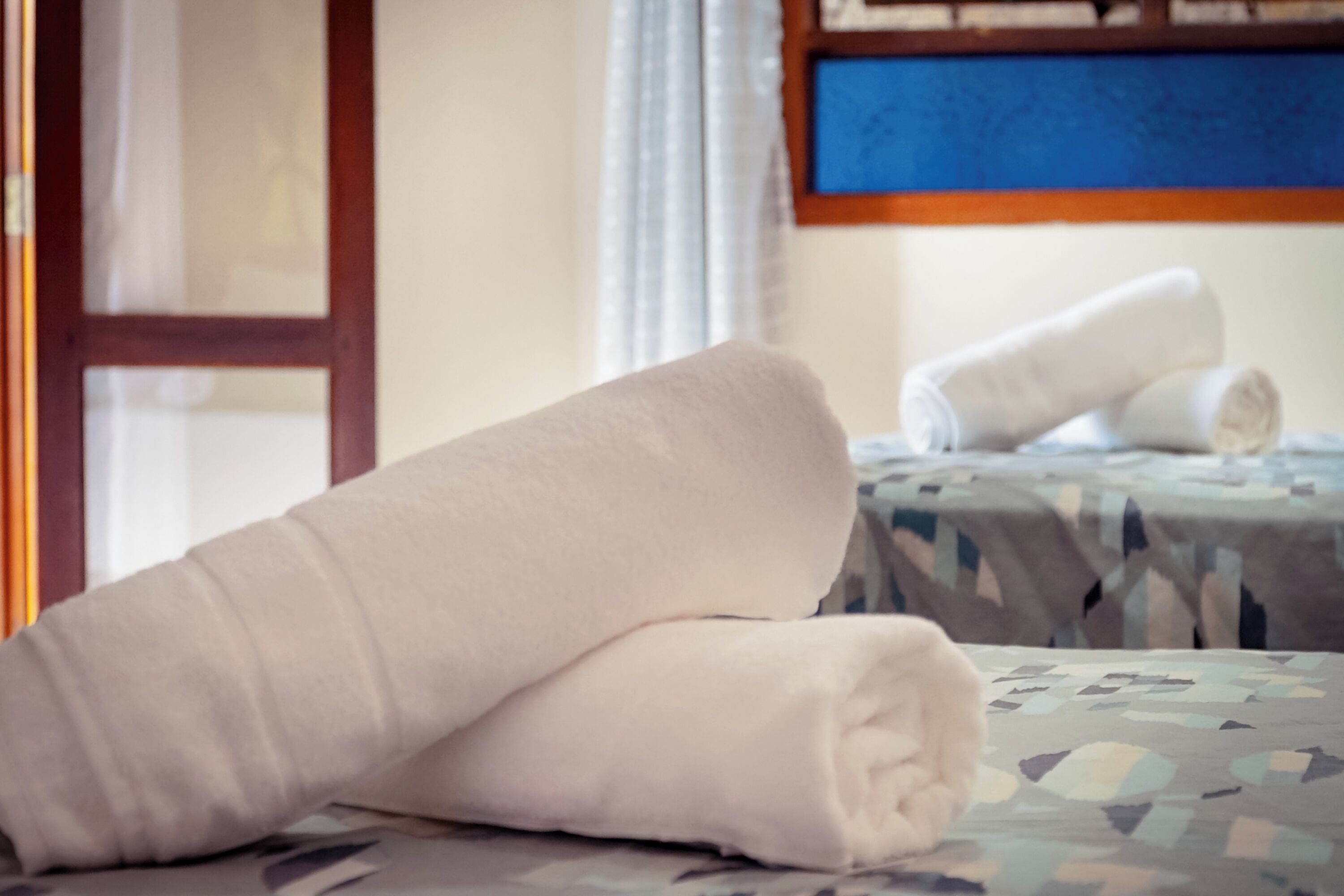 Un lit bien fait, avec une couvre-lit à motifs et une serviette blanche roulée posée dessus.
