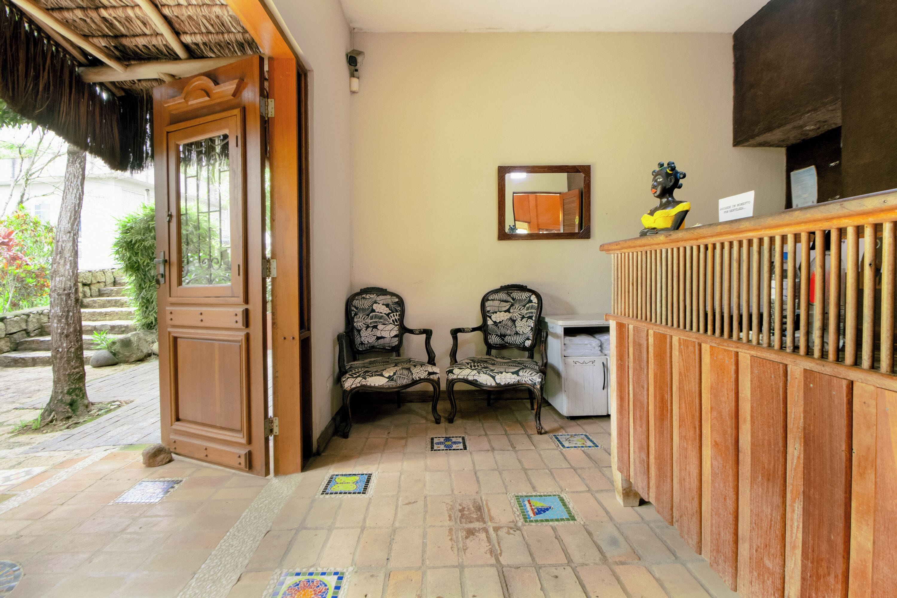 Un área de recepción con un mostrador de madera, dos sillas estampadas, piso de baldosas y una puerta que da al exterior.