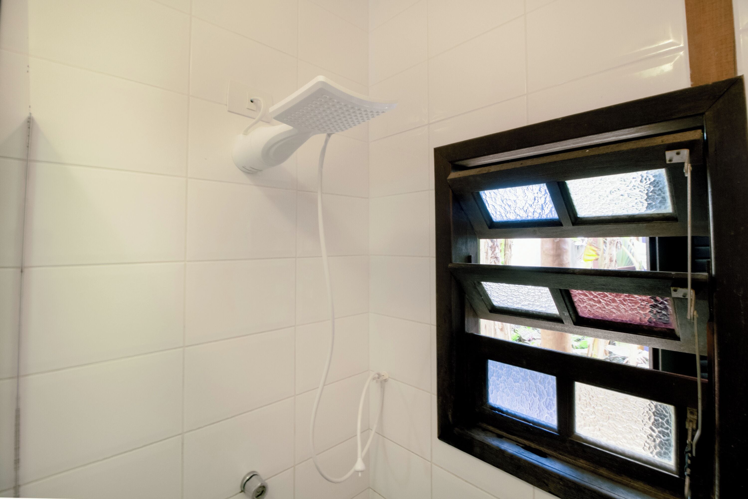 A shower with a white handheld showerhead and a window with patterned glass.