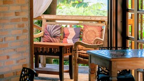 Un banco de madera con cojines, una mesa y vistas a la vegetación a través de una ventana.