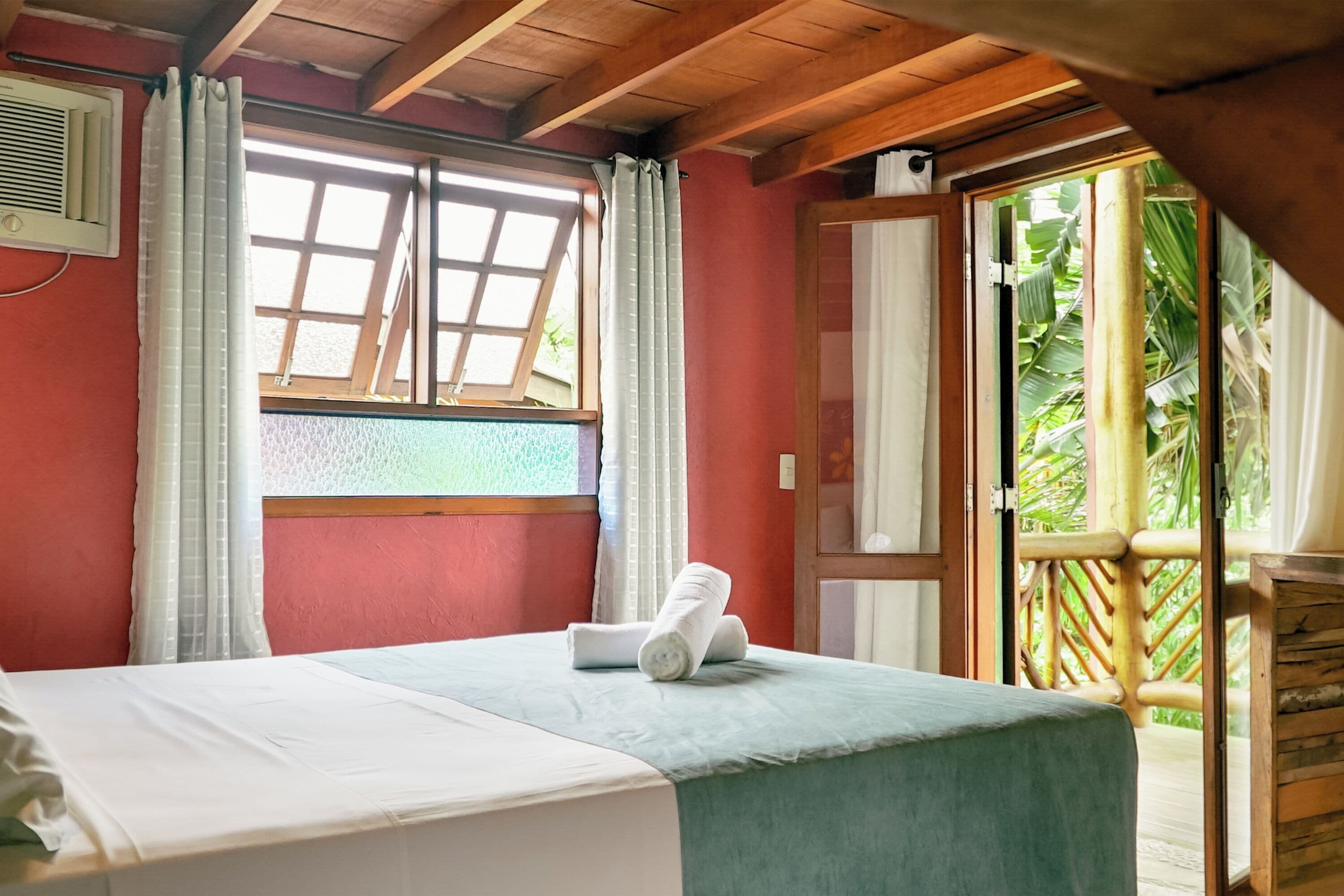A room with a bed, a window with curtains, and a view of greenery outside.