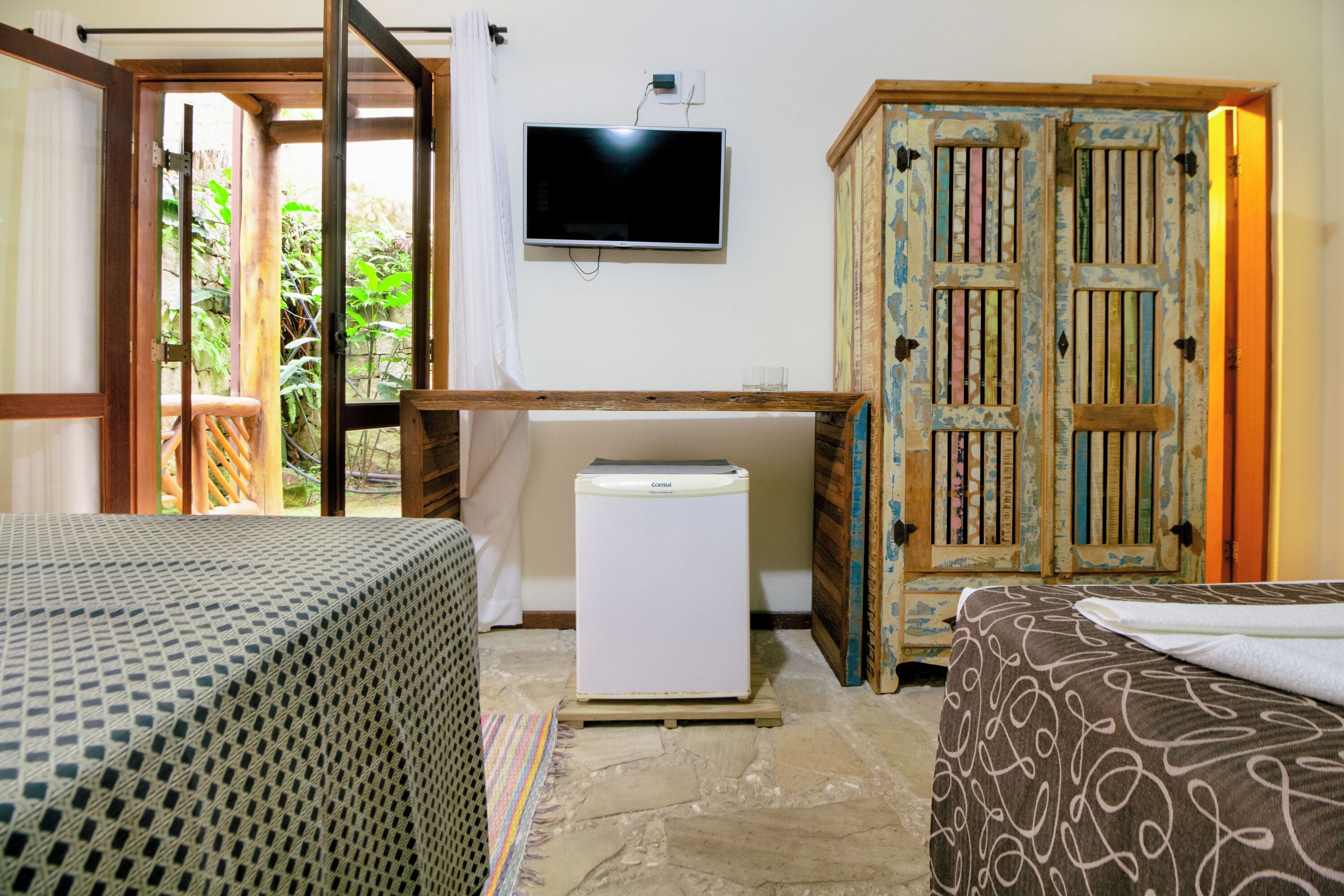 A room with a bed, a small white refrigerator, a television on the wall, and a wooden cabinet.