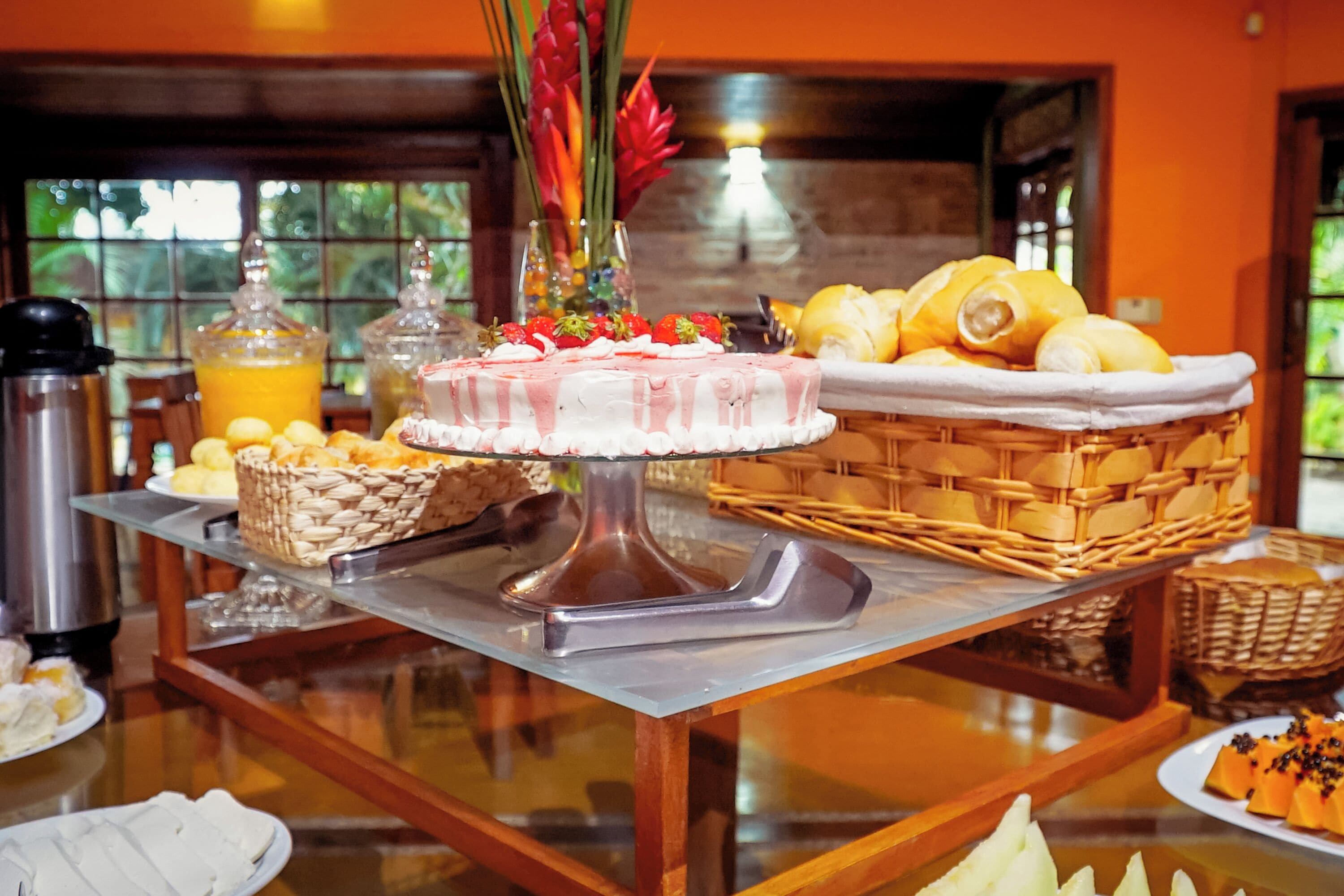 Una mesa de bufé con diversos alimentos, como pastel, frutas y pan.