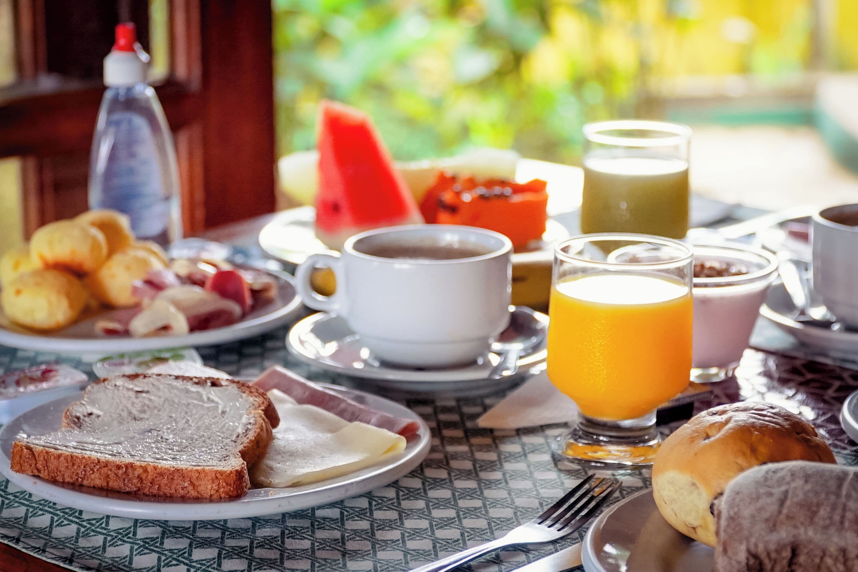 A breakfast table with plates of toast, eggs, and fruit, along with cups of coffee and orange juice.