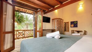 Una habitación con cama, televisor, aparador de madera y balcón con vista a vegetación.