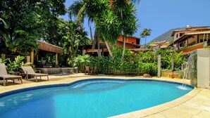 Una piscina con sillones de descanso, rodeada de plantas tropicales y una montaña al fondo.