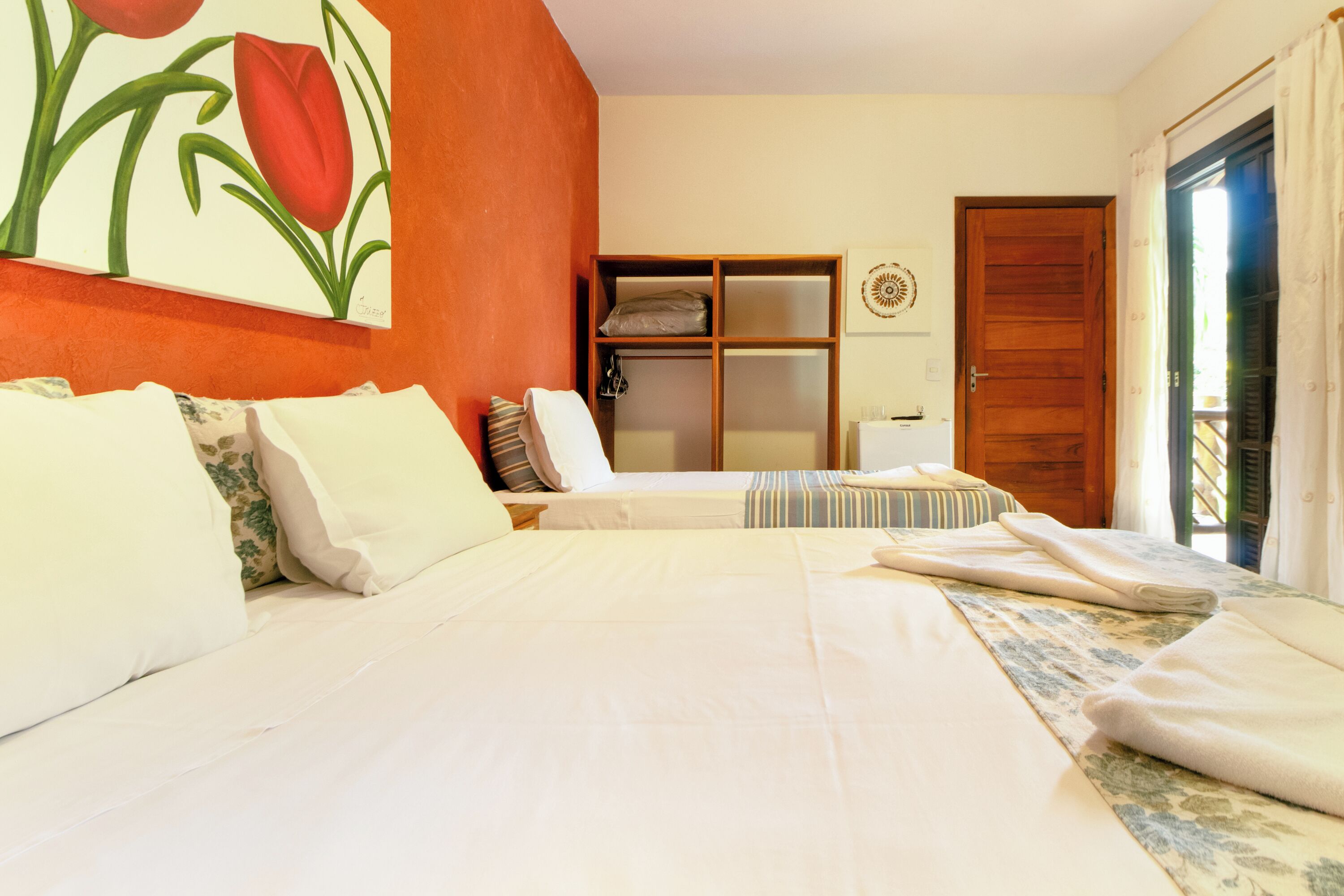 A hotel room with a large bed, a wooden wardrobe, a small table, and a window with curtains.