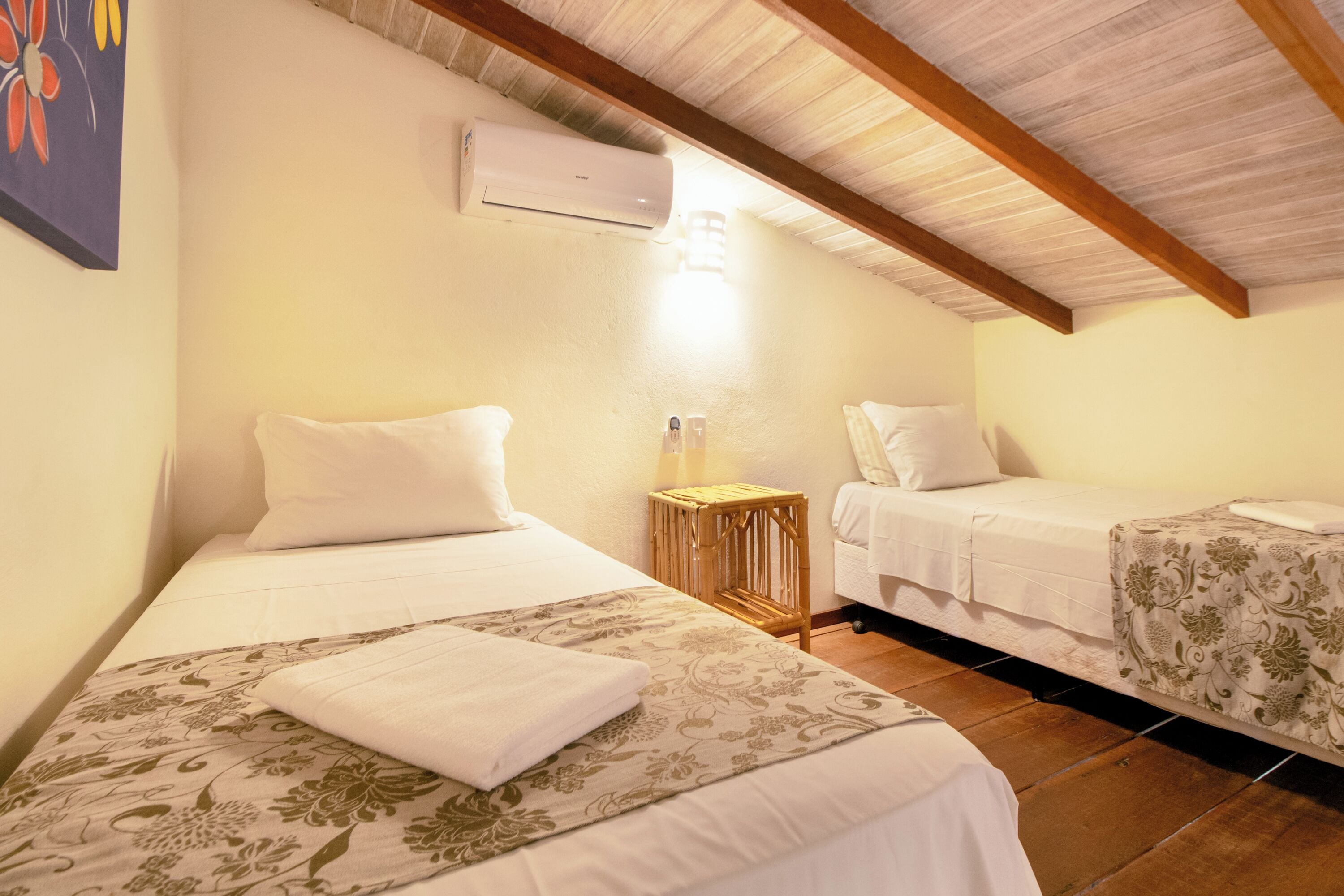 A bedroom with two beds, a wooden ceiling, an air conditioner, and a bedside lamp.