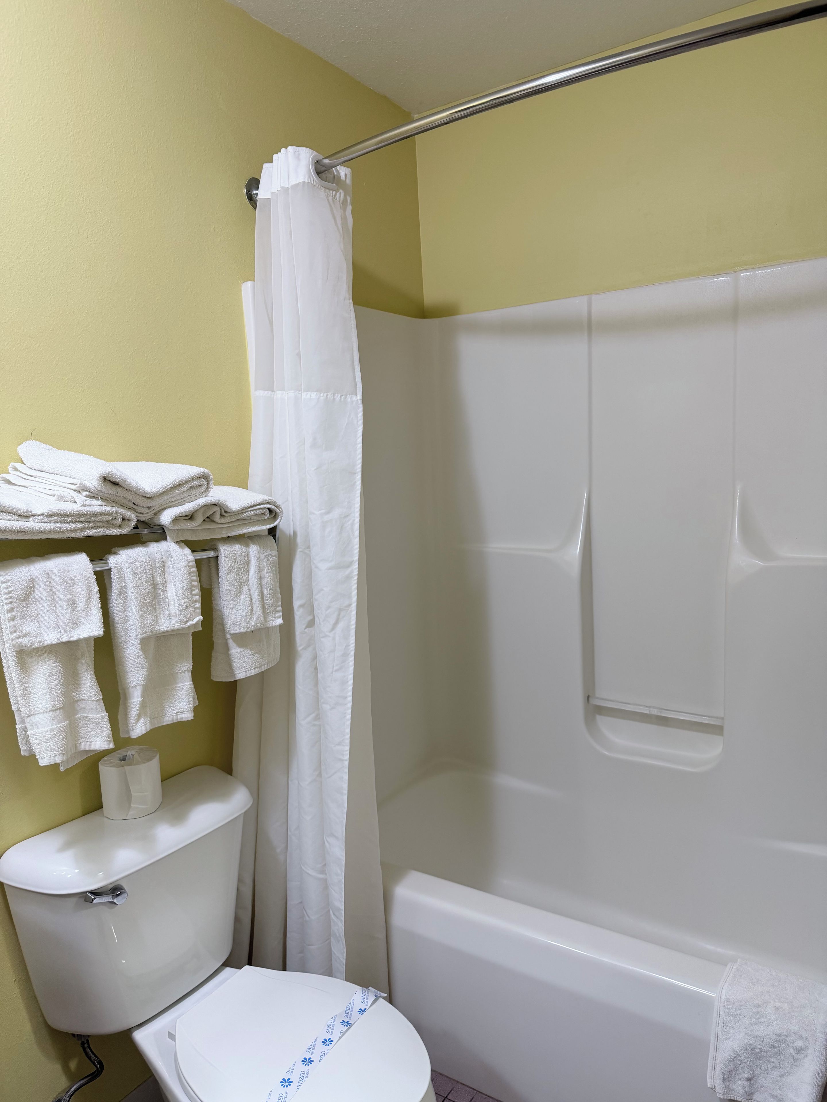 Ein Badezimmer mit Toilette, Dusche und einem Stapel weißer Handtücher auf einem Regal.