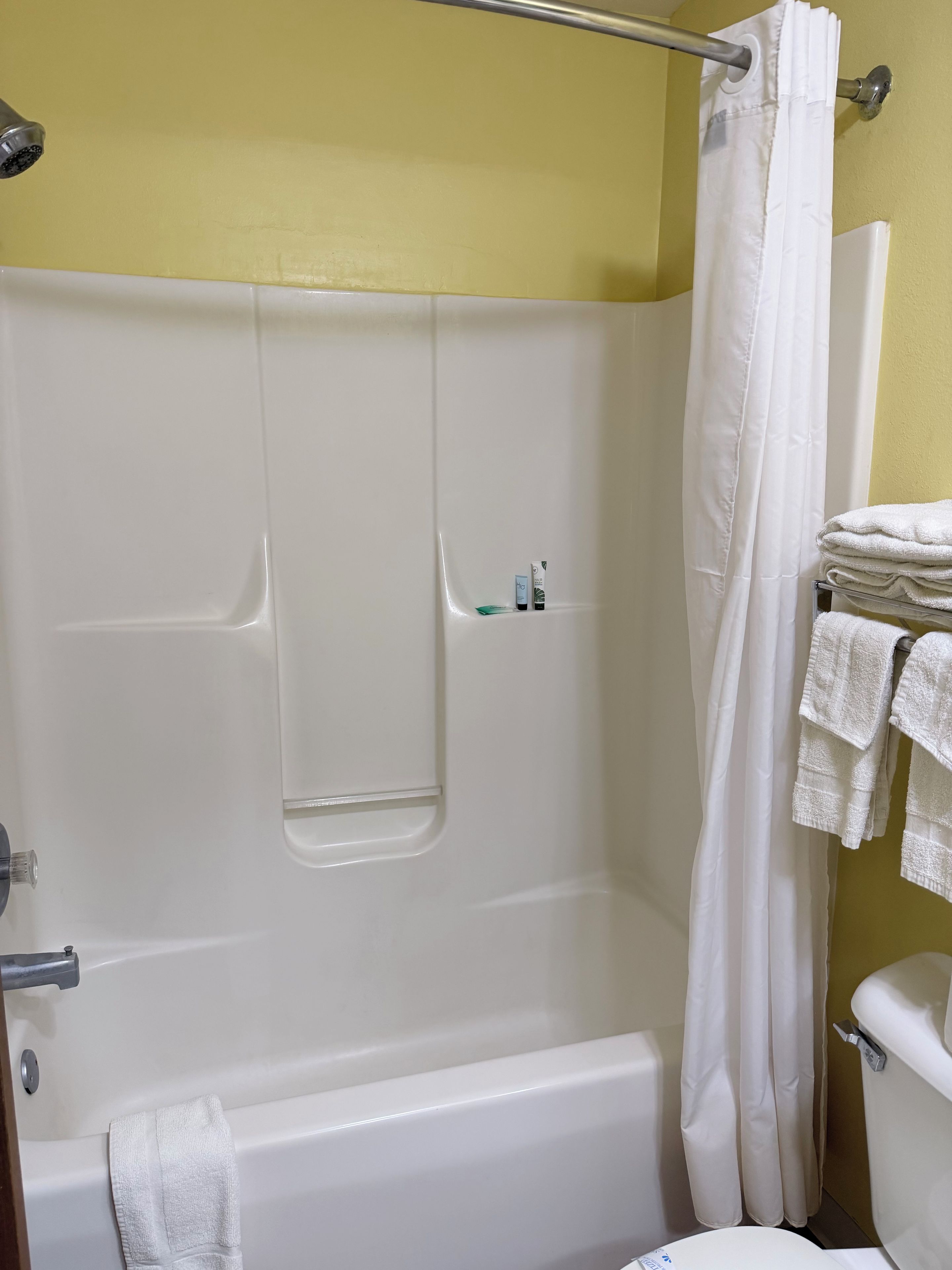 A bathroom with a bathtub, a shower curtain, and a toilet. There are towels stacked on a rack.
