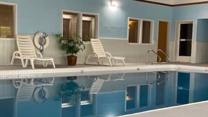 Une piscine intérieure à l’eau claire, entourée de chaises longues blanches et agrémentée d’une plante en pot.