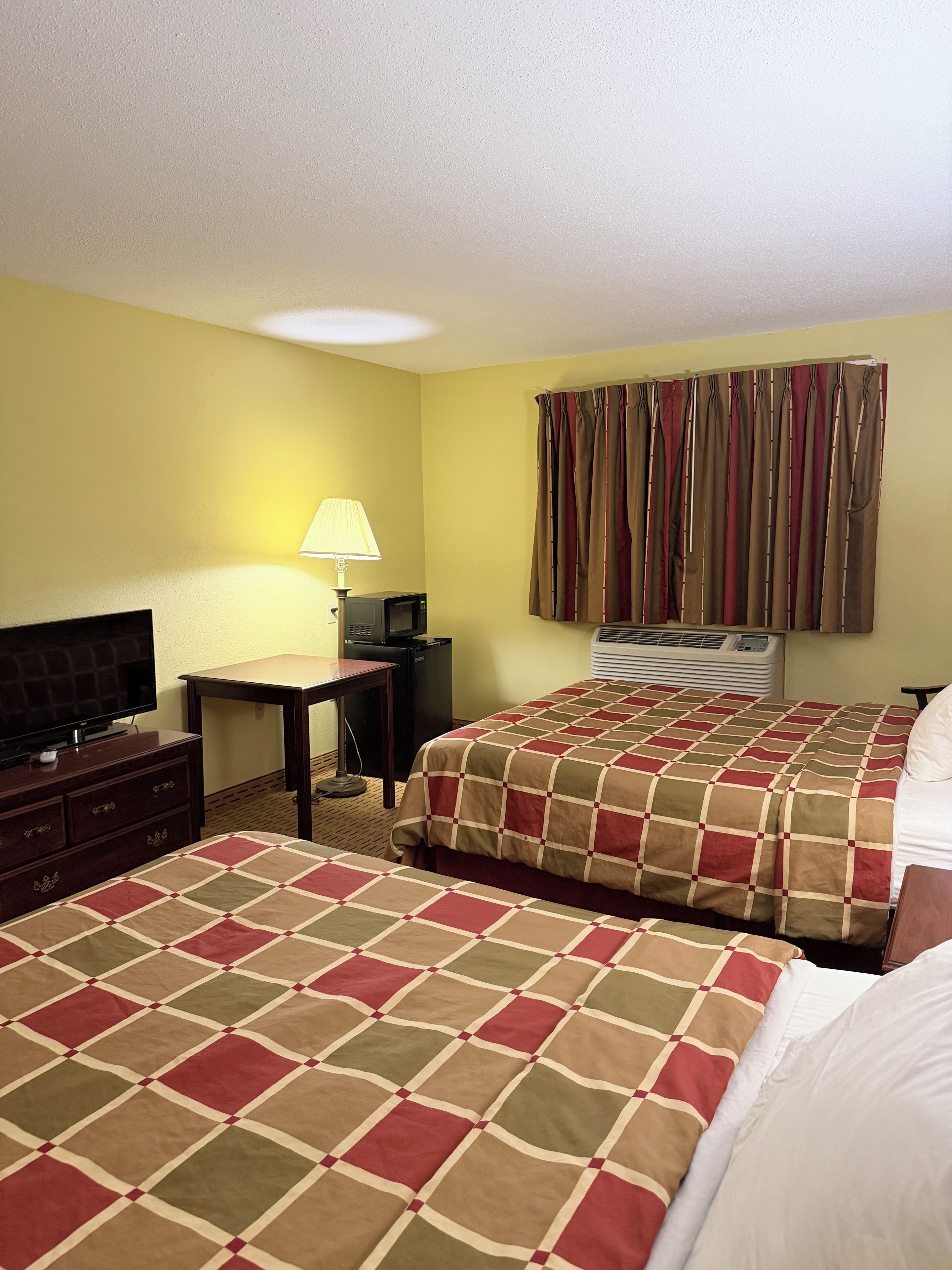 Una habitación de hotel con dos camas, televisión, escritorio y lámpara.
