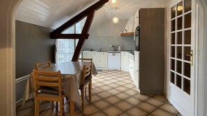 A dining area with a table and chairs, a kitchen in the background, and a large arched doorway. - Petit Gite Lavie - Lucq-de-bearn (LUCQ-DE-BEARN)