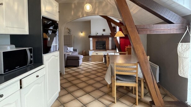 A kitchen with white cabinets, a microwave, and a dining area with a table and chairs. - Petit Gite Lavie - Lucq-de-bearn (LUCQ-DE-BEARN)
