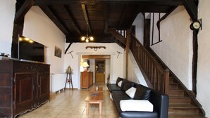 A spacious living room with a wooden staircase, a sofa, a coffee table, and a TV. - Otxania - Juxue - Gîte (JUXUE)