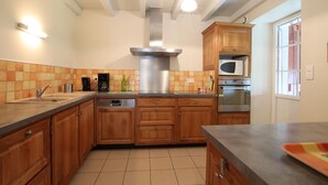 A kitchen with wooden cabinets, a stainless steel range hood, a microwave, and a dishwasher. - Otxania - Juxue - Gîte (JUXUE)