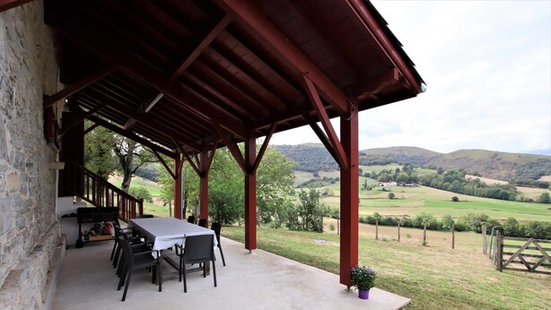 A covered outdoor area with a table and chairs, a stone wall, and a view of rolling hills. - Otxania - Juxue - Gîte (JUXUE)