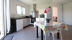 Une cuisine compacte dotée d’appareils électroménagers modernes, un coin repas avec une table et des chaises, et une grande fenêtre qui laisse entrer la lumière naturelle.