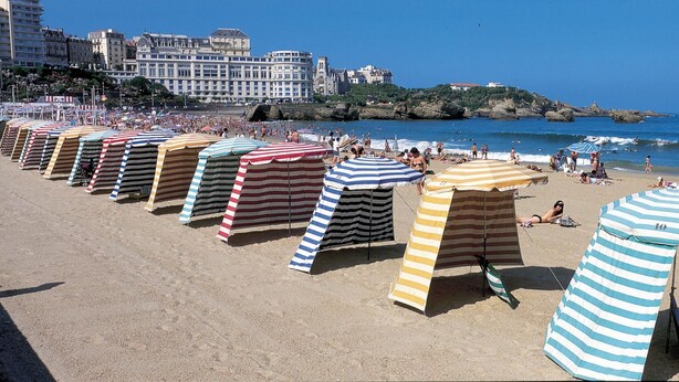 Une plage avec des parasols rayés et des gens qui prennent un bain de soleil.
