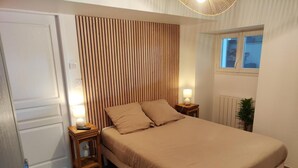 Ein Schlafzimmer mit Holzschrankgitter, einem Bett mit beige farbenen Bettwaren, zwei Nachttischen mit Lampen, einem Fenster mit Jalousien und einer Heizung.
