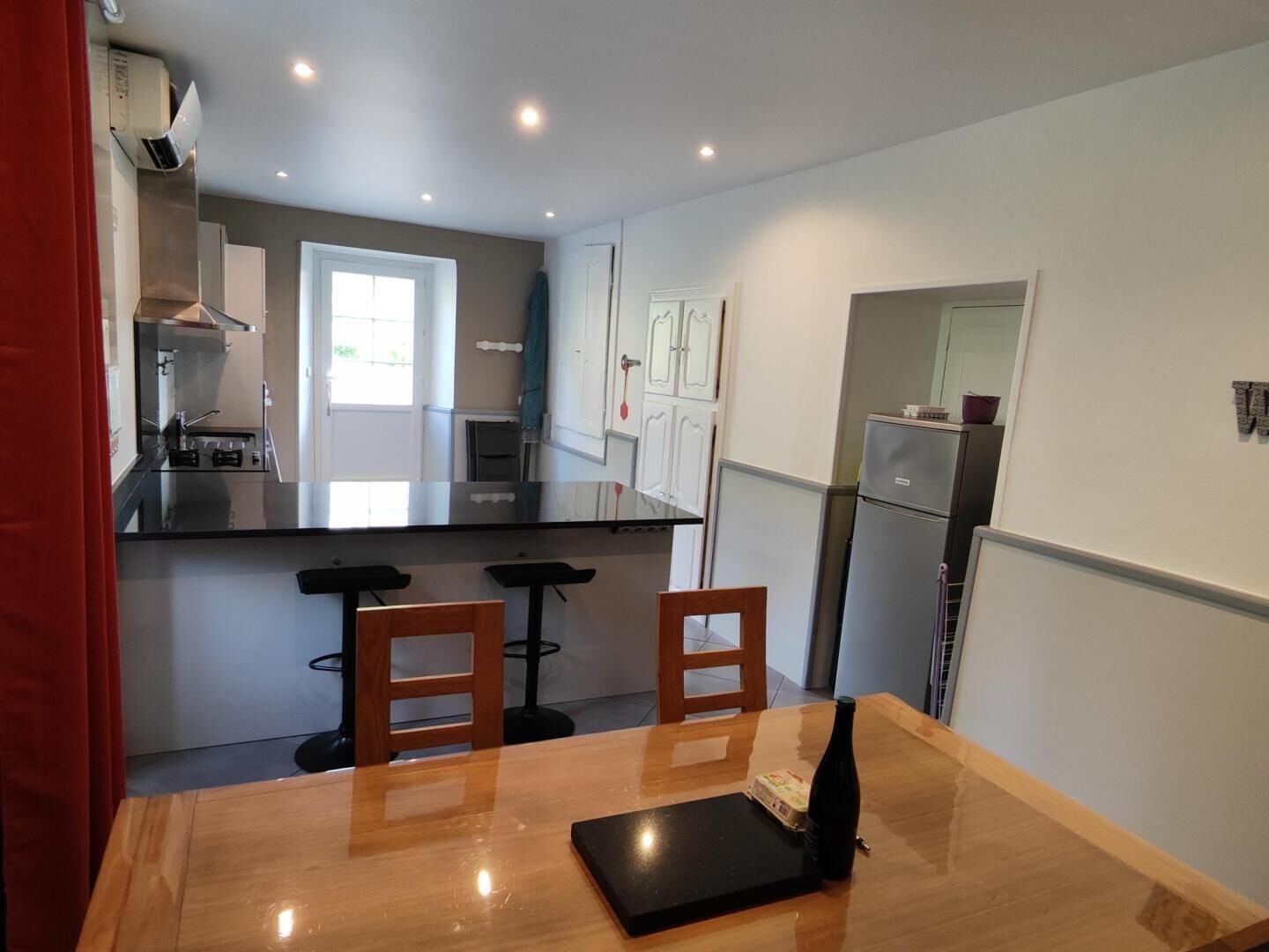 A compact kitchen with a central island, two bar stools, a dining table, and a refrigerator.