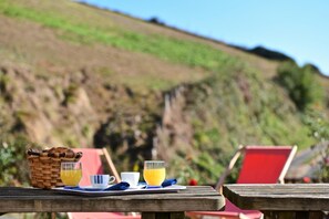 A breakfast setup with a basket, two cups, and a glass of orange juice on a wooden table with a red chair in the background. - SARAHANDIA - ALDUDES (LES-ALDUDES)