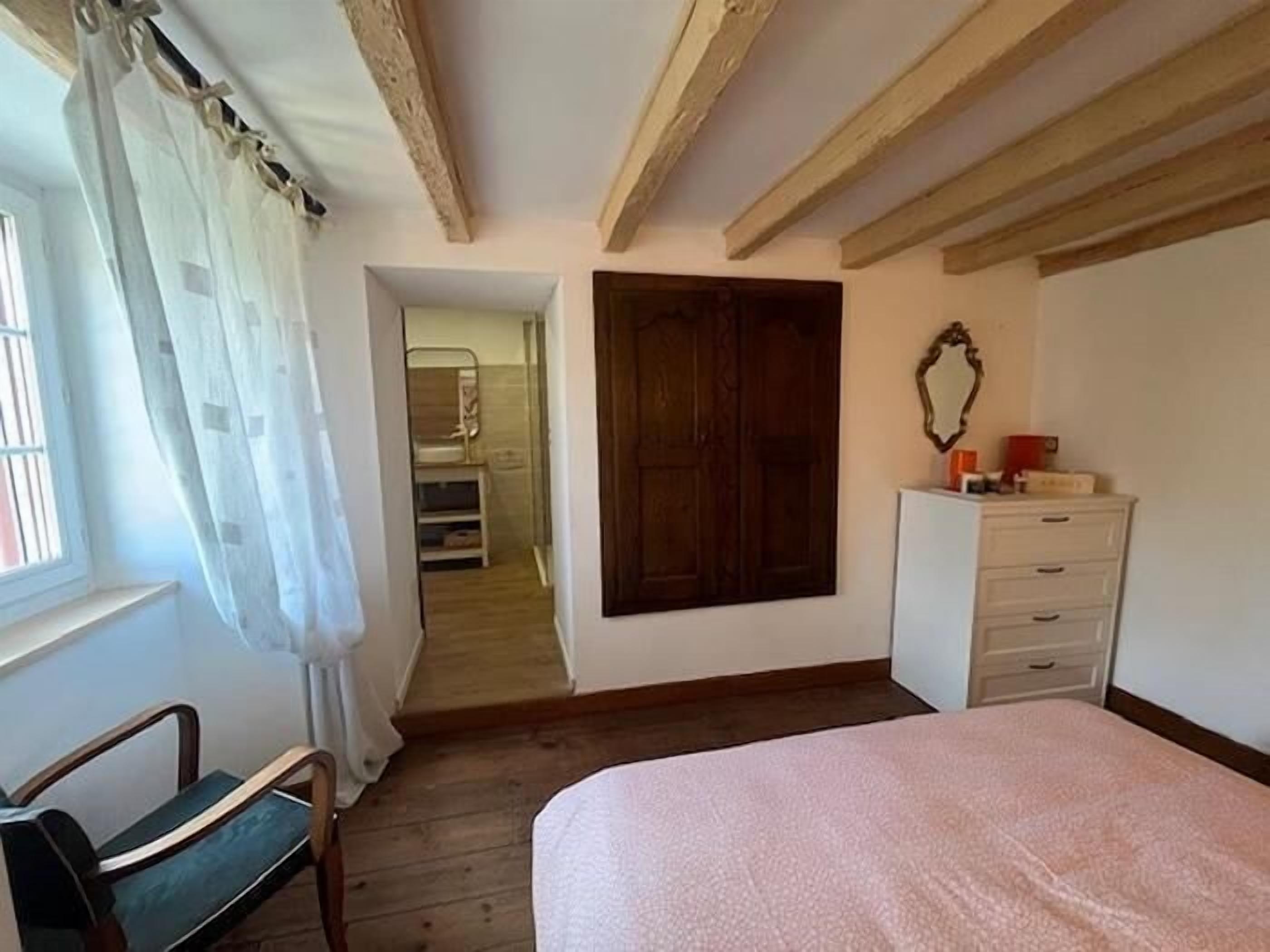 Een slaapkamer met een bed, een dressoir, een spiegel en een raam met gordijnen.