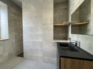 Une salle de bain moderne avec des carreaux gris, un lavabo noir, des meubles en bois et un miroir au-dessus du lavabo.