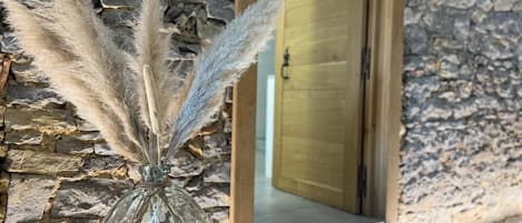 A stone wall with a glass vase containing pampas grass.